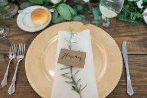 Rustic Wedding Day Place Setting with Gold Plate Charger on Wooden Feasting Table with Greenery | Tampa Wedding Planner Inspire Weddings and Events