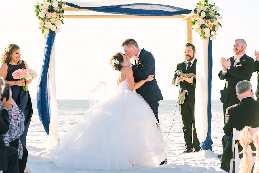 Clearwater Beach Wedding Ceremony Bride and Groom First Kiss Under Bamboo Arch With Ivory and Navy Linens and Blush and Ivory Roses | Tampa Bay Wedding Venue Hilton Clearwater Beach | Linens by Over The Top Rental Linens