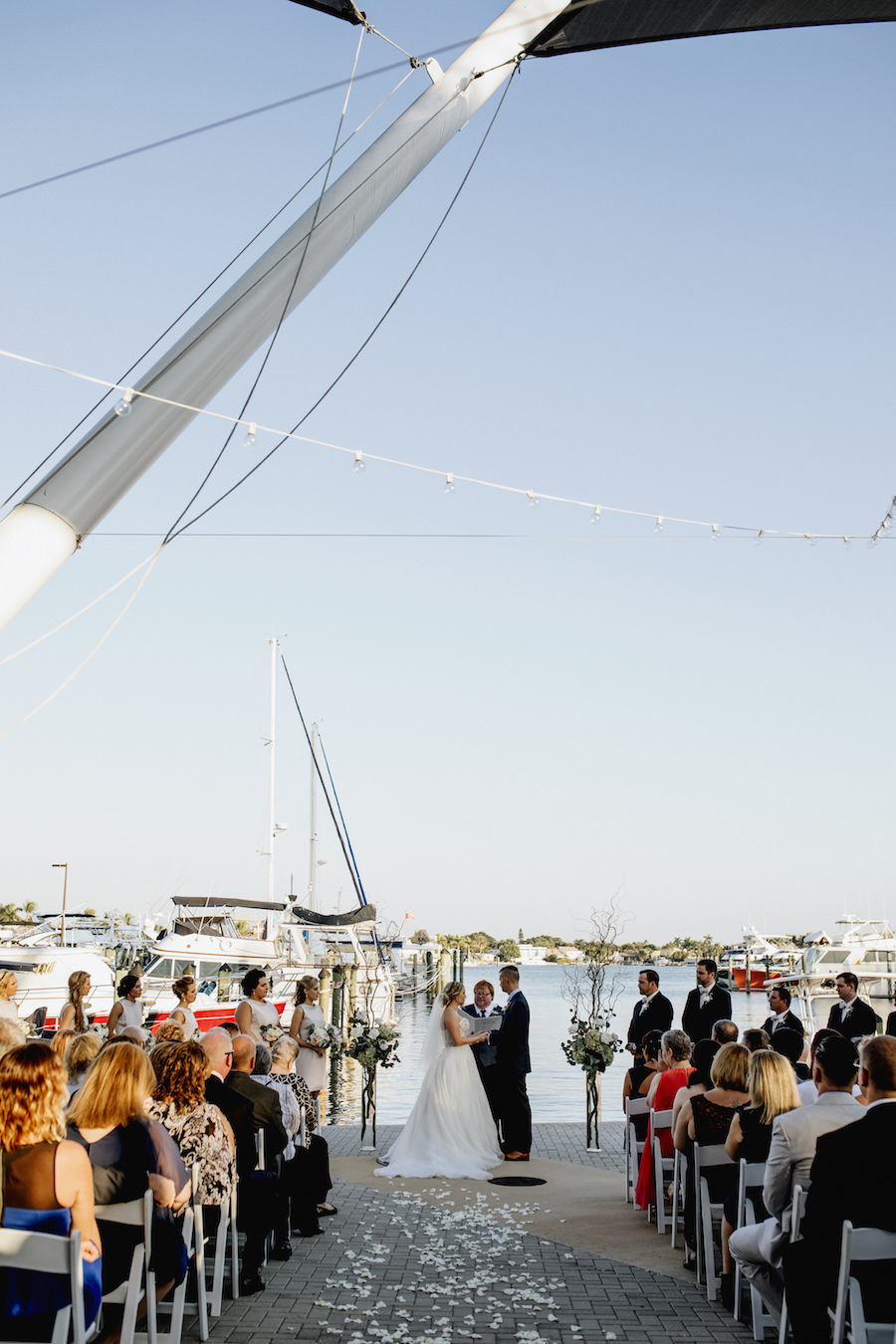Outdoor Sarasota Wedding Ceremony with Bride and Groom Between Tall Glass Vases with Branches, Ivory Florals and Greenery | Wedding Venue Sarasota Yacht Club | Tampa Bay Wedding Planner NK Productions