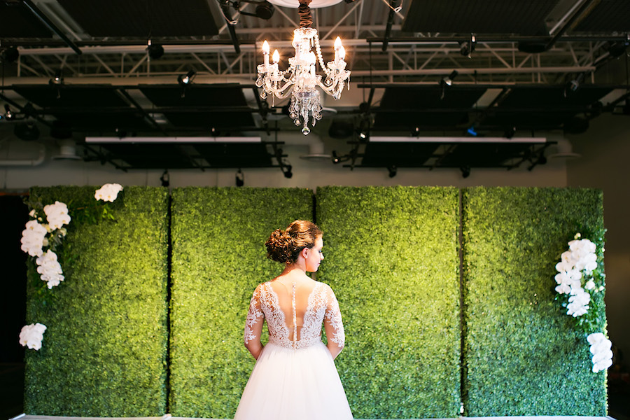 Nude Illusion Lace Wedding Dress with Sleeves and Greenery Hedge Backdrop Wall and Hanging Chandelier | Tampa Bay Bridal Shop Isabel O'Neil Bridal | Rental and Decor Company A Chair Affair | Wedding Photographer Limelight Photography | Lighting Nature Coast Entertainment Services