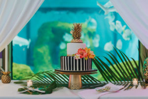 Two Tier Black and White Striped Wedding Cake with Gold Pinapple Topper and Bright Orange and Pink Tropical Flowers