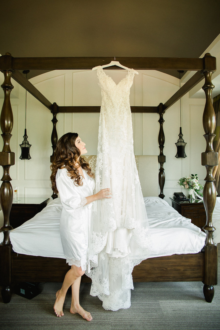 Bride Looking at Gown Hanging From Four Post Bed Wedding Portrait | St. Petersburg Wedding Venue The Birchwood | Tampa Bay Wedding Photographer Ailyn La Torre Photography