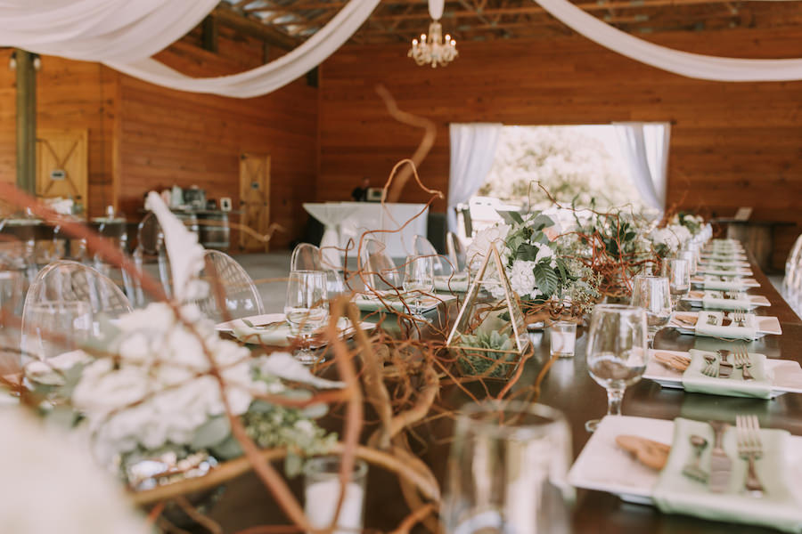 Outdoor Barn Wedding Reception Feasting Table with Rustic Wood Decor with White Hydrangea and Succulent Greenery Decor Centerpieces with Clear Ghost Chairs | Sarasota Wedding Planner Jennifer Matteo Event Planning