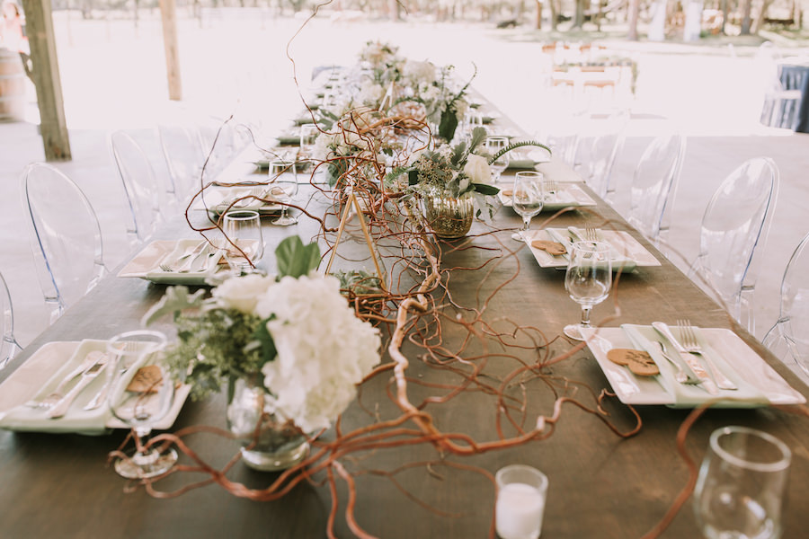Outdoor Barn Wedding Reception Feasting Table with Rustic Wood Decor with White Hydrangea and Greenery Decor Centerpieces with Clear Ghost Chairs | Sarasota Wedding Planner Jennifer Matteo Event Planning