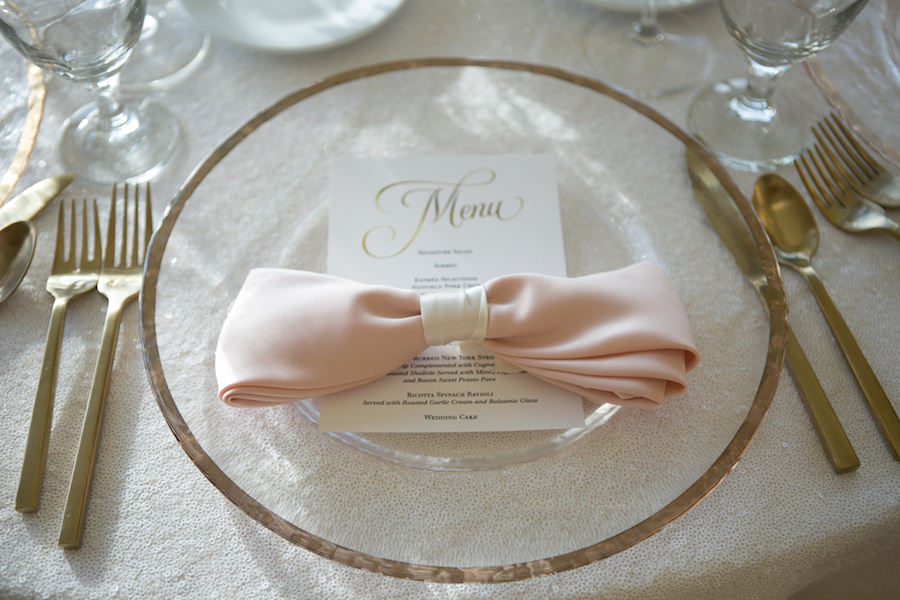 Blush Ivory and Gold Table Setting with Blush Linen Napkin Tied in Bow and Black and Gold Wedding Menu with Gold Silverware and Gold-Rimmed Glass Chargers | Rentals A Chair Affair | Linens by Gabro Event Services | Wedding Venue The Tampa Club | Tampa Wedding Photographer Carrie Wildes Photography | Tampa Wedding Stationery A & P Designs