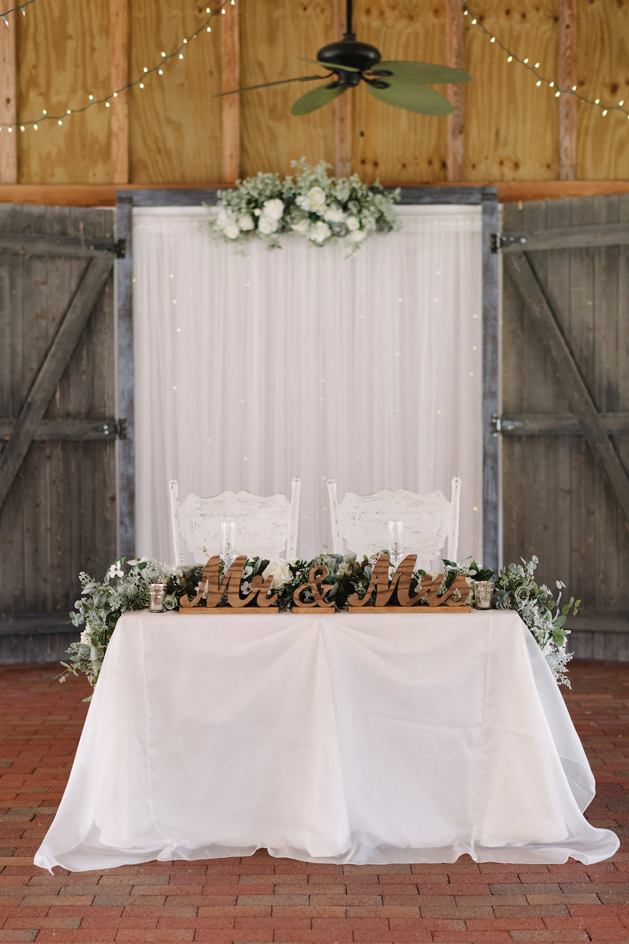 Rustic Wedding Sweetheart Table with White Linens, Cascading Dusty Miller Greenery and Wooden Mr and Mrs Centerpiece at Tampa Bay Wedding Venue Cross Creek Ranch