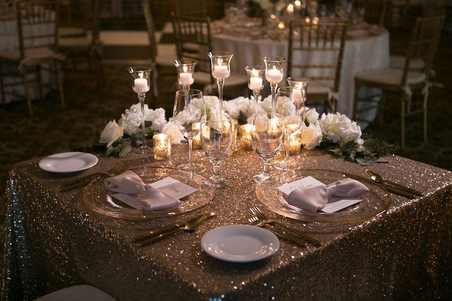 Gold and Ivory Wedding Sweetheart Table with Gold Glitter Linens and White Roses with Gold Mercury Tea Light Candles and Medium Tea Light White Candles in Glass Candle Holders with Gold Chiavari Chairs | Tampa Wedding Rentals A Chair Affair | Tampa Wedding Linens Gabro Event Services | Wedding Venue The Tampa Club | Wedding Photographer Carrie Wildes Photography | Tampa Bay Wedding Florist Northside Florist
