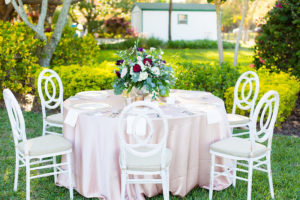 Garden Party Wedding With Blush Satin Tablecloths, Ivory and Burgundy Floral Wedding Centerpieces and Rustic Ivory Wooden Chairs | Tampa Wedding Photographer Kera Photography