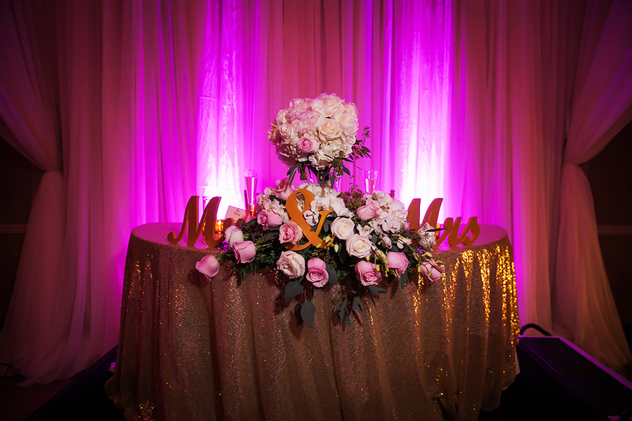 Wedding Sweetheart Table with Gold Sequin Specialty Linens and Pink and Ivory Roses with Cascading Greenery against Pink Uplighting | St Pete Wedding Photographer Limelight Photography