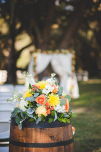 Fall Inspired Wedding Ceremony Floral Decor with Orange, Yellow Flowers, Greenery Accents and Wine Barrels