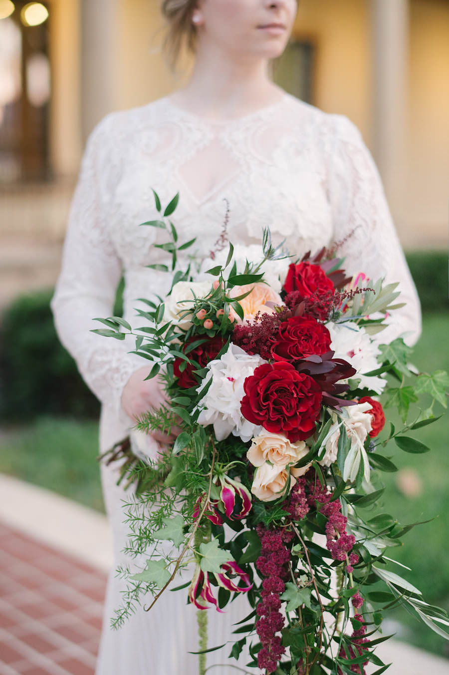 Bridal Portrait in Lace Long Sleeved White Wedding Dress with Pleated Bottom and Fall Inspired Bouquet of Red, Fuchsia, Ivory and Peach Florals with Greenery