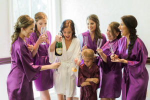 Bride and Bridesmaids Getting Ready Wedding Portrait in White and Purple Silk Robes with Personalized Champagne Glasses