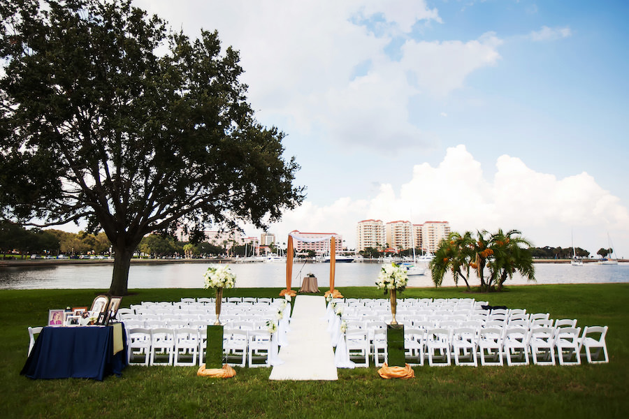 White Wedding Chair Aisle Runner Ceremony Flowers with Aisle Runner and Draped Altar and Tall White, Green and Gold Elegant Wedding Ceremony Flowers Decor on Mirrored Pedestals | Waterfront Downtown St. Pete Wedding Ceremony Location | St. Petersburg Wedding Planner Parties a la Carte