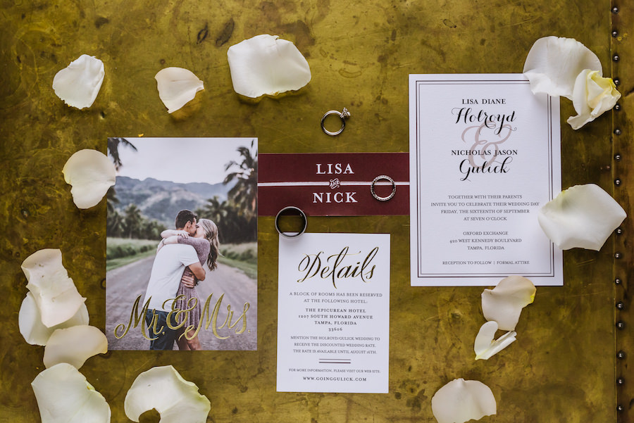 Stylish and Elegant White and Burgundy Bordeaux Wedding Invitation Suite Detail Photo with Rose Petals and Wedding Engagement Rings and Bands