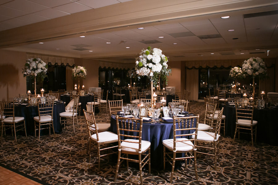 Classic Gold and Navy Wedding Reception Decor with Gold Chiavari Chairs and Tall White Rose, Hydrangea, and Greenery Centerpieces with Navy Blue Linens | Tampa Bay Wedding Venue The Tampa Club | Northside Florist