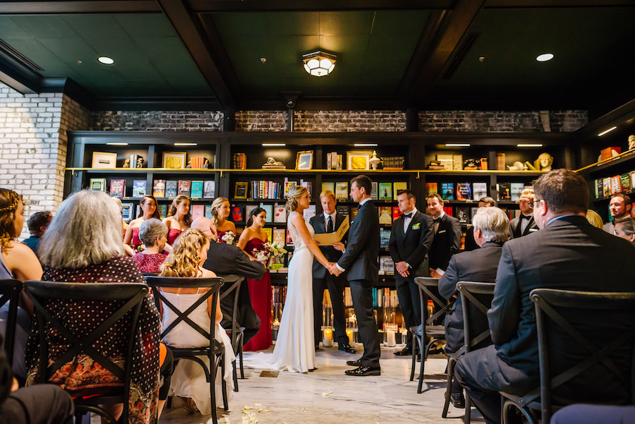 Elegant Rustic Wedding Ceremony Portrait with Bookshelves, Black Wooden Chairs, Votive Candles in Tall Glass Vases, Bordeaux Bridesmaids Dresses and Martina Liana Wedding Dress | Tampa Bay Wedding Venue Oxford Exchange