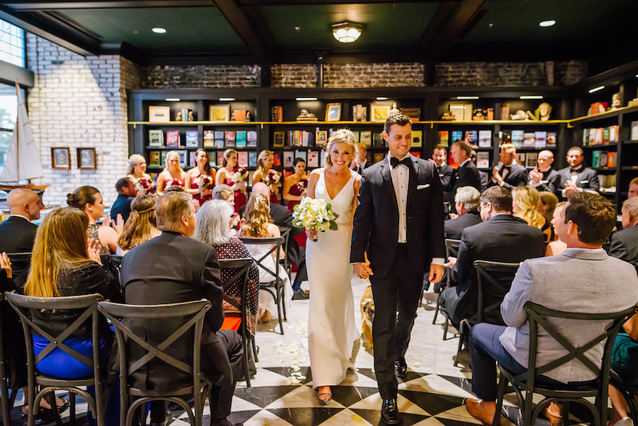 Elegant Rustic Wedding Ceremony Portrait with Bookshelves, Black Wooden Chairs, Bordeaux Bridesmaids Dresses, white floral bouquet with Greenery, and Martina Liana Wedding Dress with Silver Open-Toed shoes | Tampa Bay Wedding Venue Oxford Exchange