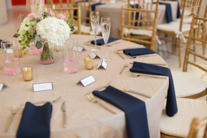 Modern Elegant Reception Table Decor with Low White Hydrangeas, Pink Roses, and Greenery Centerpieces and Blush Linen with Navy Blue Napkins, Gold Mercury Votive Candle Holders and Gold Chiavari Chairs