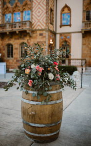 Rustic Barrel Wedding Ceremony Flower Arrangement with Wild Greenery and White, Pink, and Orange Roses
