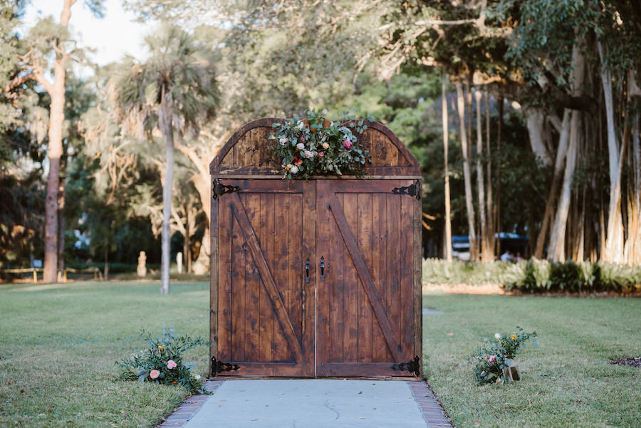 Outdoor Wedding Ceremony Entrance Decor with Rustic Antique Wooden Door, and Natural Greenery with Pink and Orange Flowers | Sarasota Wedding Planner NK Productions