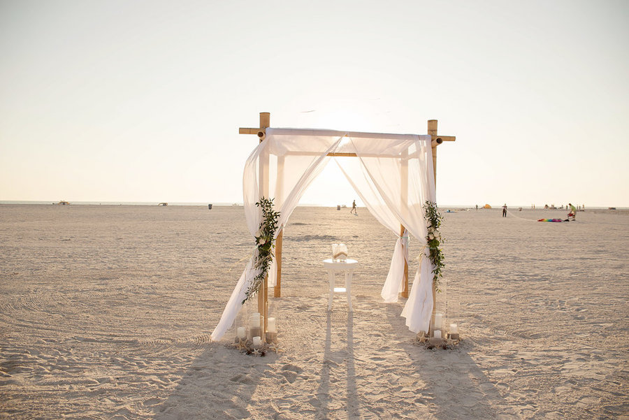 Beach Ceremony Wedding Arch with White Drapery and Natural Beach Inspired Flowers and Pillar Candles | Tampa Bay Wedding