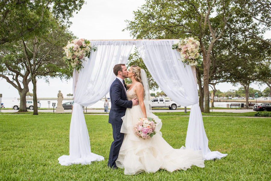 Outdoor Waterfront Wedding Ceremony Portrait with White Fabric Curtain Arch, Blush Pink and Ivory Rose Bouquets | Cream Beaded Voluminous Layered Ball Gown Wedding Dress and Navy Suit | Downtown St Petersburg Wedding Venue North Straub Park | Tampa Bay Wedding Planner Special Moments Event Planning