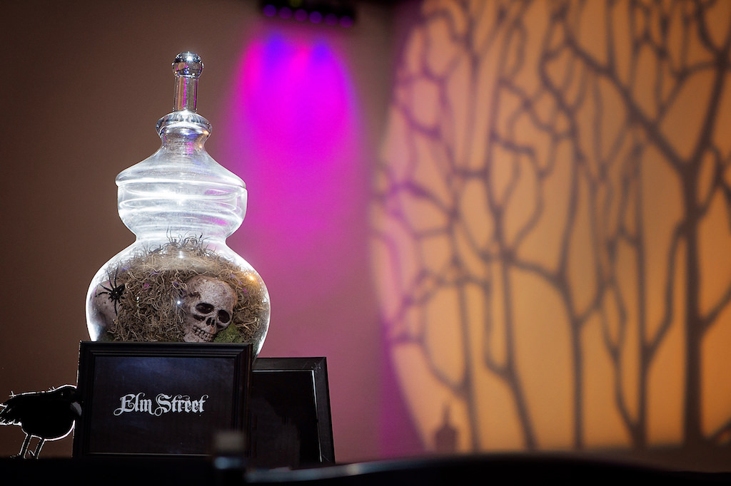 Halloween Themed Wedding Reception Table Decor with Antique Glass Jar with Skull Centerpiece, Classic Horror Movie Table Names, Raven, and Spooky Tree Shadow Projection | Sarasota Wedding DJ and Lighting Nature Coast Entertainment Services