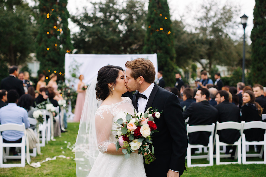 Ceremony Exit Bride and Groom Portrait at Outdoor Tampa Bay Garden Wedding Venue The Palmetto Club with White, Blush, and Red Rose Bouquet with Greenery and White Folding Chairs