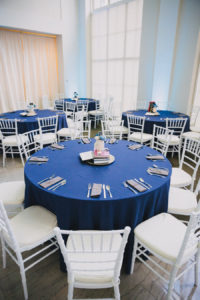 Modern Wedding Reception Round Table Decor with White Chiavari Chairs, Gray Napkins, Blue Linen, and Creative Books and Guestbook with Pens Centerpiece