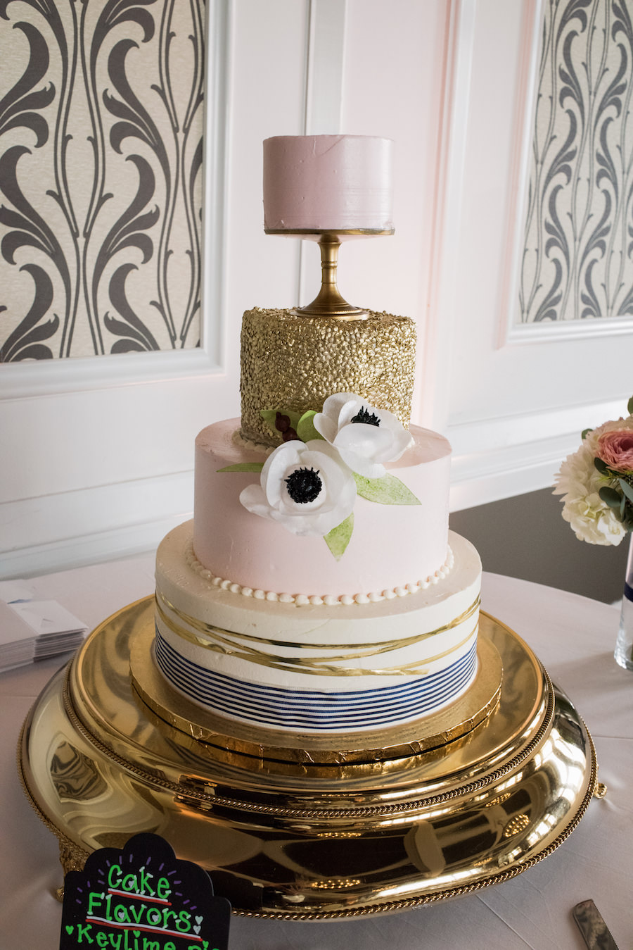 Four Tiered Gold and Navy Wedding Cake from Tampa Bay Bakery A Piece of Cake with Stripes, Glitter and Mini Cake Tray Topper and Anemones on Gold Platter