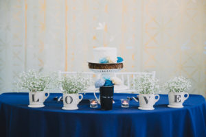 Bride and Groom Wedding Reception Blue and White Table Decor with LOVE Ceramic Letter Coffee Mugs with Babys Breath, Small Blue and White Flowers, and Small Round White Wedding Cake on White Cake Stand