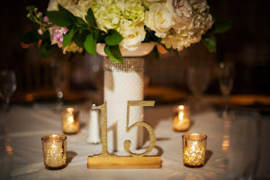 Gold and White Wedding Reception Table Decor with Glitter Gold Table Number, Low White and Blush Pink Centerpiece in Rhinestone Vase, and Gold Mercury Votives