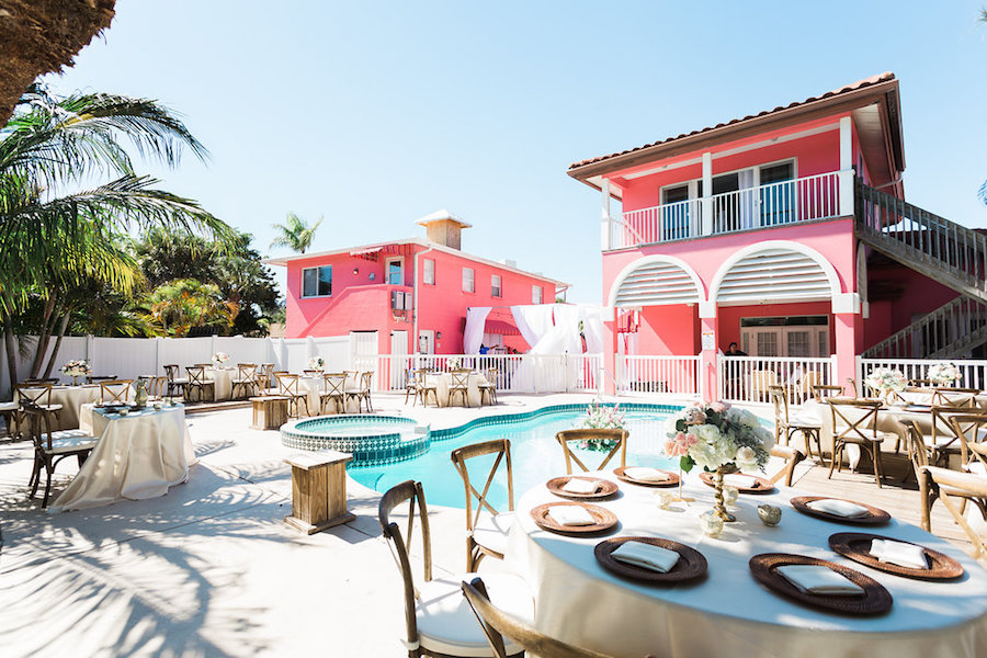 Reception Decor for Retro Inspired Beach Villa Poolside Wedding with Wooden Chairs and Floating White and Pink Tropical Bouquet with Wild Greenery | Siesta Key Wedding Venue Tropical Breeze Resort | Sarasota Wedding Planner Parties A La Carte