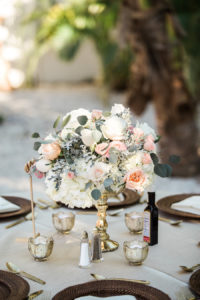 Outdoor Beach Wedding Reception Table Decor with Tall White Blush and Greenery Centerpiece in Gold Vase, Brown Woven Chargers and Natural Linen, and Silver Mercury Votives