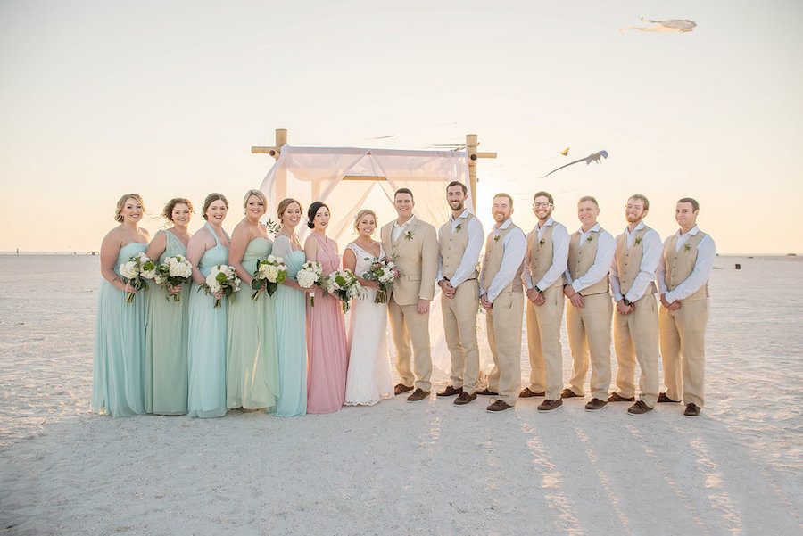Beach Wedding Party Portrait with David's Bridal Mismatched Bridesmaids Dresses in Meadow, Mint, and Blush with White Bouquets with Greenery, Groomsmen in Tan Suits with Pastel Blue Shirts | Treasure Island Romantic Beach Wedding | Tampa Bay Florida Wedding Photographer Kristen Marie Photography