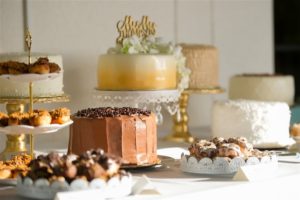 Desert Table with Multiple Cakes and Treats on Gold and White Platters and Gold Mr and Mrs Cake Topper