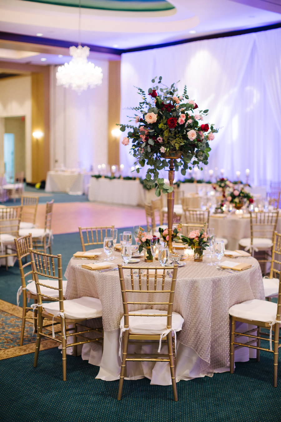 Elegant Ivory and Gray Reception Decor at Tampa Bay Wedding Venue The Palmetto Club with Tall Centerpiece with Blush and Red Roses and Greenery, and Gold Chiavari Chairs