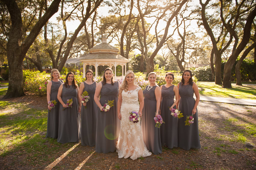 Outdoor Garden Bridal Party Portrait with Cream Floral Lace Allure Bridal Wedding Dress, Long Gray Alfred Angelo Bridesmaids Dresses, and Pink, Purple and White Bouquets with Ferns and Greenery | Downtown Tampa Wedding Venue The Tampa Club