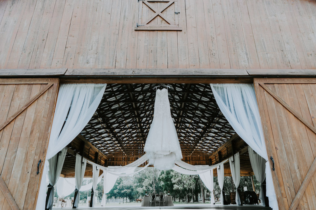 Rustic Barn Wedding Reception with White Draping and Wedding Dress on Hanger