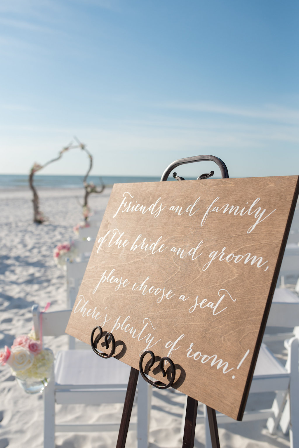 Hand-painted Wooden Welcome Sign at Beach Wedding Ceremony with Natural Driftwood Arch, Folding White Chairs with White and Pink Flowers | St Petersburg Wedding Venue The Don Cesar