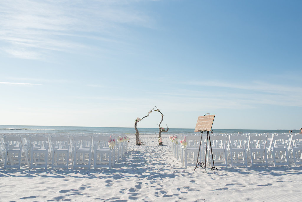 Wooden Welcome Sign at Beach Wedding Ceremony with Natural Driftwood Arch, Folding White Chairs with White and Pink Flowers | St Petersburg Wedding Venue The Don Cesar
