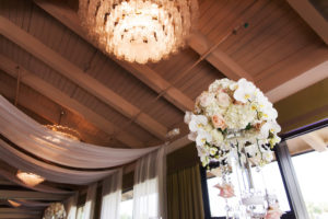 Gold Champagne and Blush Timeless Elegance Wedding Reception Decor with White Ceiling Drapery and Tall Orchid, Blush Rose and Hydrangea Centerpiece with Hanging Beads in Tall Cylinder Vase