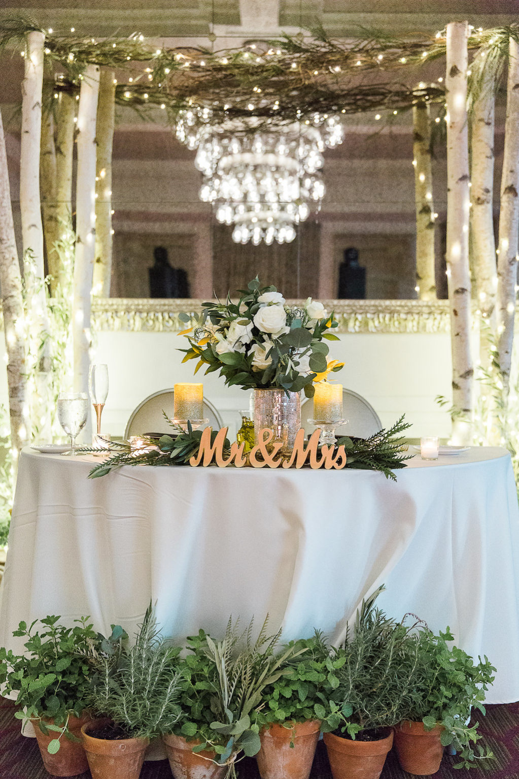 Natural Organic Wedding Reception Sweetheart Bride and Groom Table with Stylish Gold Mr and Mrs Letters, Herbs Growing in Ceramic Pots, Greenery and Silver Pillar Candle Table Decor, and White Birch Tree and Branches with String Lights Arch | Downtown St Pete Hotel Wedding Venue The Birchwood