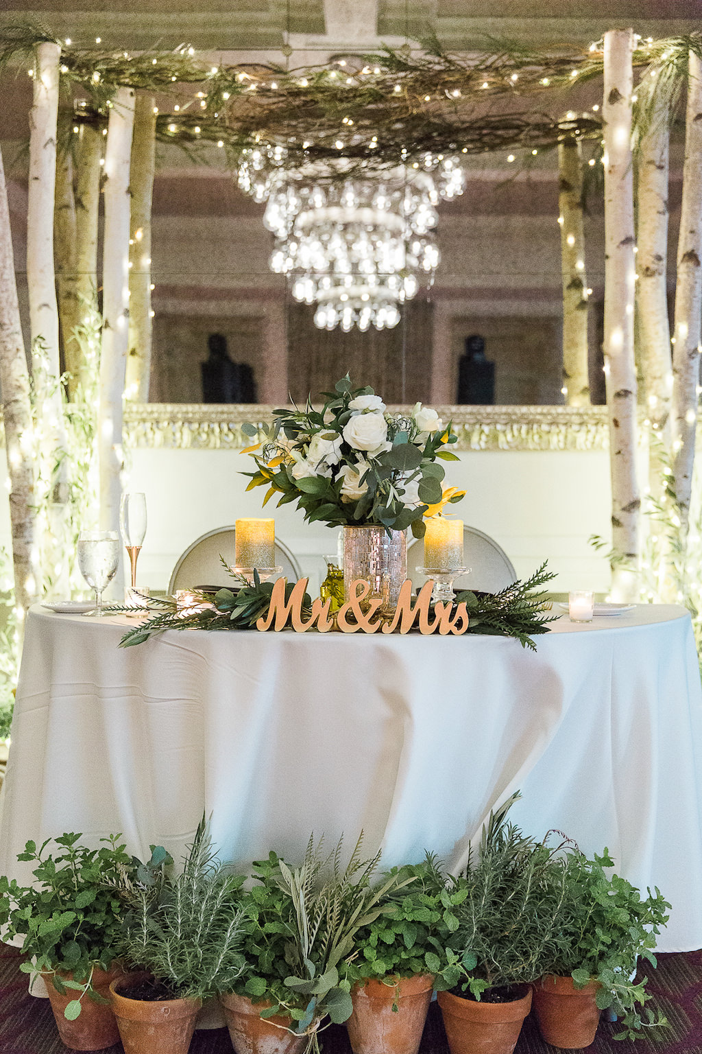 Natural Organic Wedding Reception Sweetheart Bride and Groom Table with Stylish Gold Mr and Mrs Letters, Herbs Growing in Ceramic Pots, Greenery and Silver Pillar Candle Table Decor, and White Birch Tree and Branches with String Lights Arch | Downtown St Pete Wedding Venue The Birchwood