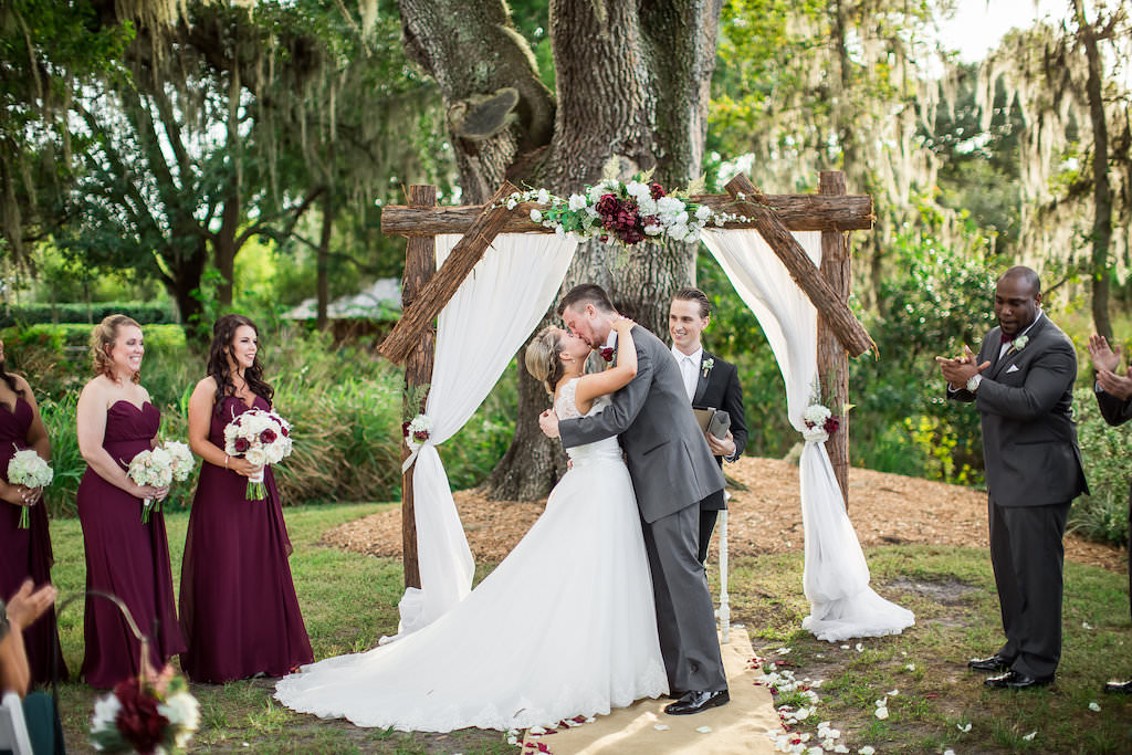 Burgundy and Cream Outdoor Rustic Farm Wedding Ceremony Portrait with Wooden Arch with Drapery and Marsala and White Bouquets and Red Bridesmaids Dresses | Tampa Bay Wedding Photography Rad Red Creative | Bridal Shop Truly Forever Bridal