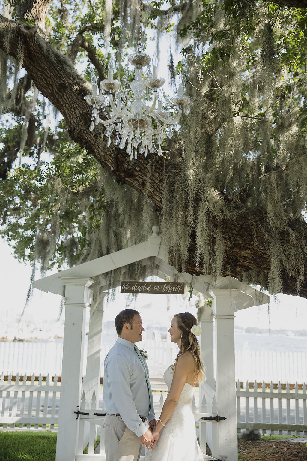 Waterfront Sarasota Wedding Ceremony Bride and Groom Portrait, Groom in Light Blue Shirt, and Vintage Chandelier in Spanish Moss Covered Oak Tree