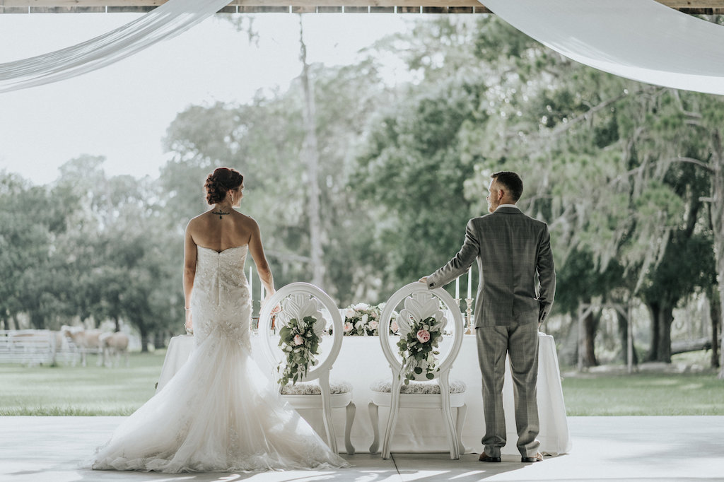 Rustic Barn Wedding Reception Bride and Groom Portrait with Antique White Chairs with Roses and Greenery and White Drapery | Sarasota Wedding Planner Kelly Kennedy Weddings and Events