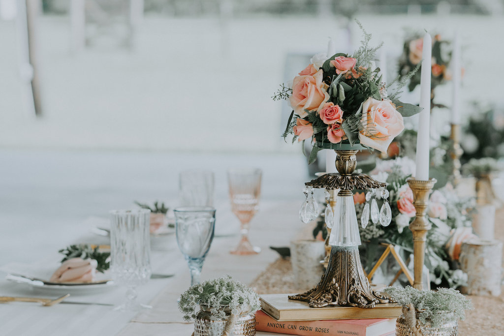 Elegant Rustic Wedding Reception Decor with Chrystal and Brass Antique Vase Centerpiece with Pink Roses and Greenery, Old Books, and Mercury Vases with Succulents, Gold Candlestick Holders, and Blush Linen, Blue and Pink Colored Champagne Glasses | Elegant Rustic Wedding Reception Decor with Crystal and Brass Antique Vase Centerpiece with Pink Roses and Greenery, Old Books, and Mercury Vases with Succulents | Elegant Rustic Wedding Reception Table Setting with Antique Gold Silverware and Painted Floral Plates, Hand-painted Leaf Place Card and Blue and Pink Menu, Blush Pink Napkin with Fern Napkin Ring | Sarasota Planner Kelly Kennedy Weddings and Events | Tampa Bay Wedding Rentals Ever After Vintage Weddings