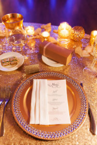 Gold Wedding Reception Table Decor with Stylish Menu, Jeweled Gold Charger, and Gold Glass Votive Candle Holders on Rose Gold Glitter LInen