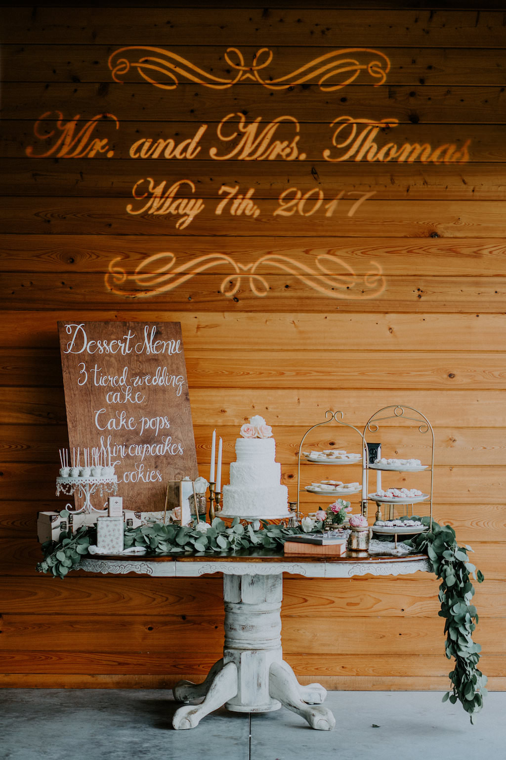 Elegant Rustic Barn Wedding Dessert Table Decor with Hand-painted Wooden Sign and Wall Decal, Three Tier Round White Wedding Cake, and Dessert Trays and Leafy Garland | Tampa Bay Wedding Planner Kelly Kennedy Weddings and Events